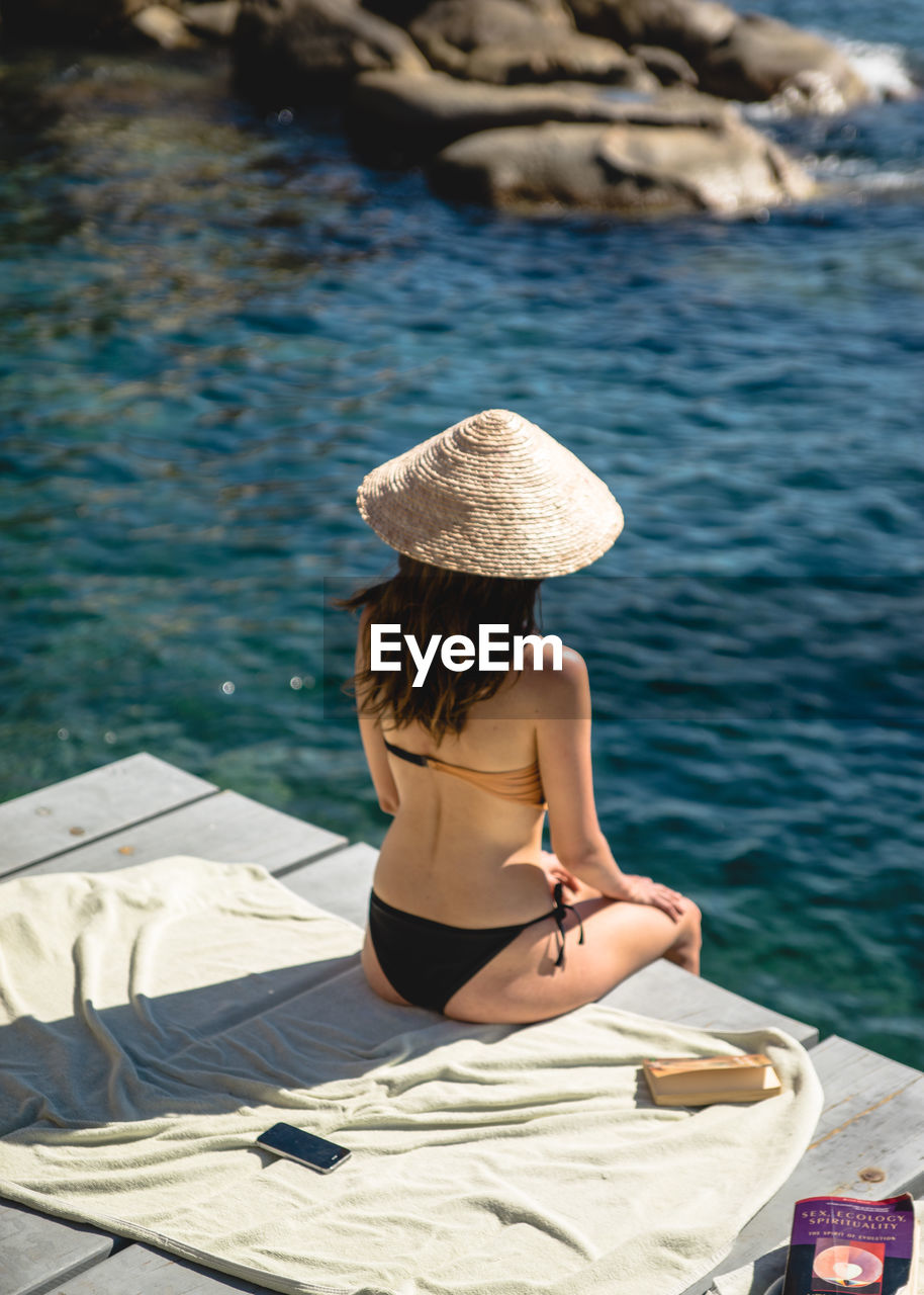 REAR VIEW OF WOMAN SITTING ON SHORE