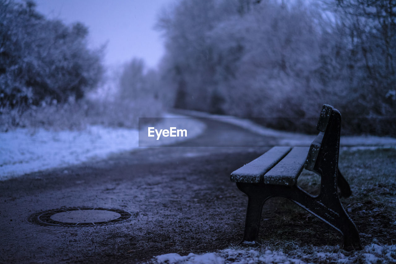 EMPTY BENCH ON SNOW FIELD DURING WINTER