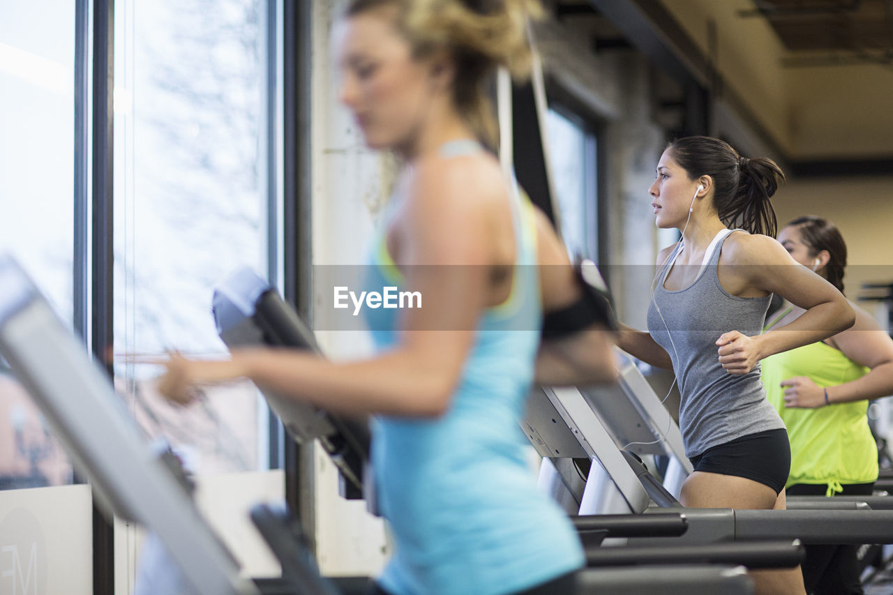 Women listening music while exercising on treadmills in gym