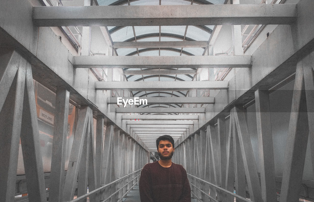 Portrait of young man standing on covered bridge