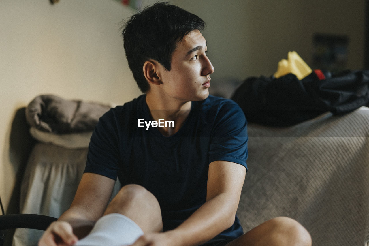 Teenage male athlete looking away while day dreaming at home