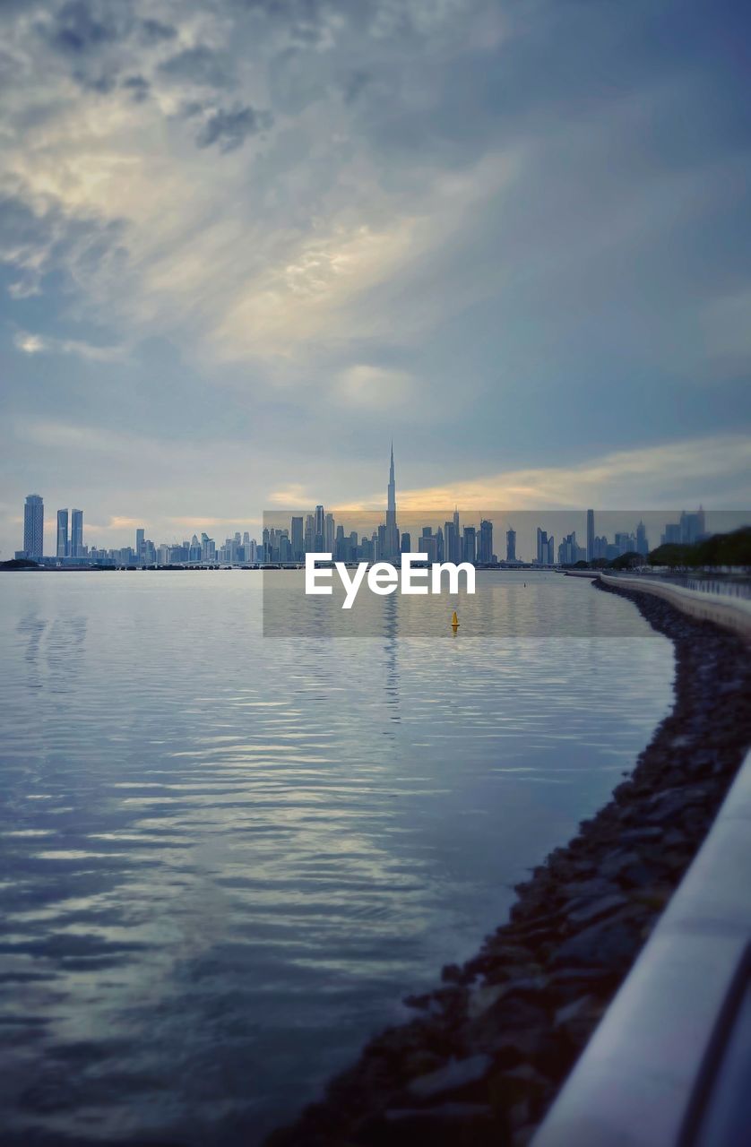 Scenic view of river by city buildings against sky