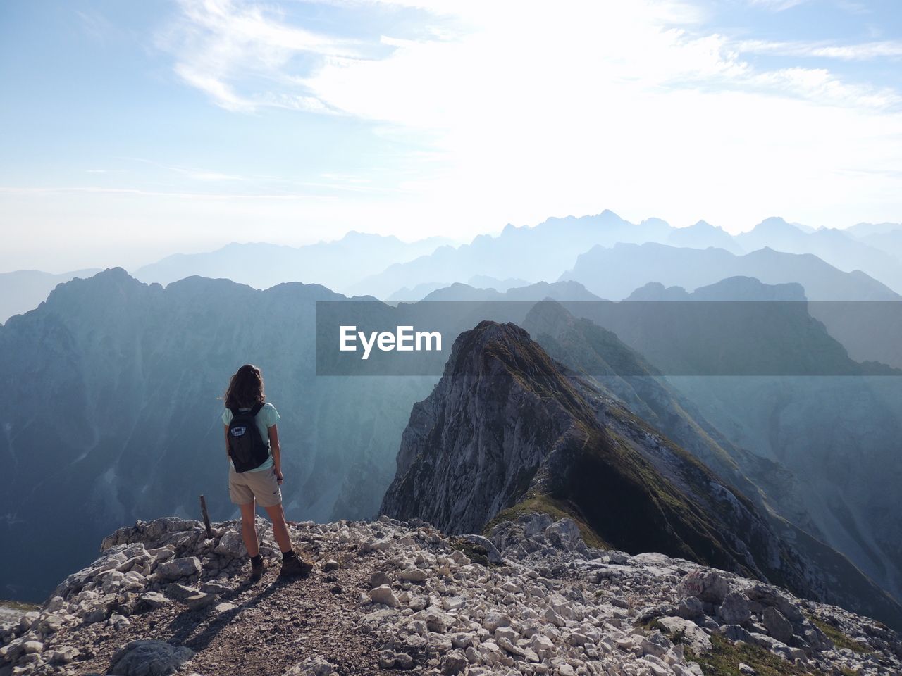 Rear view of young woman with backpack standing on mountain against sky