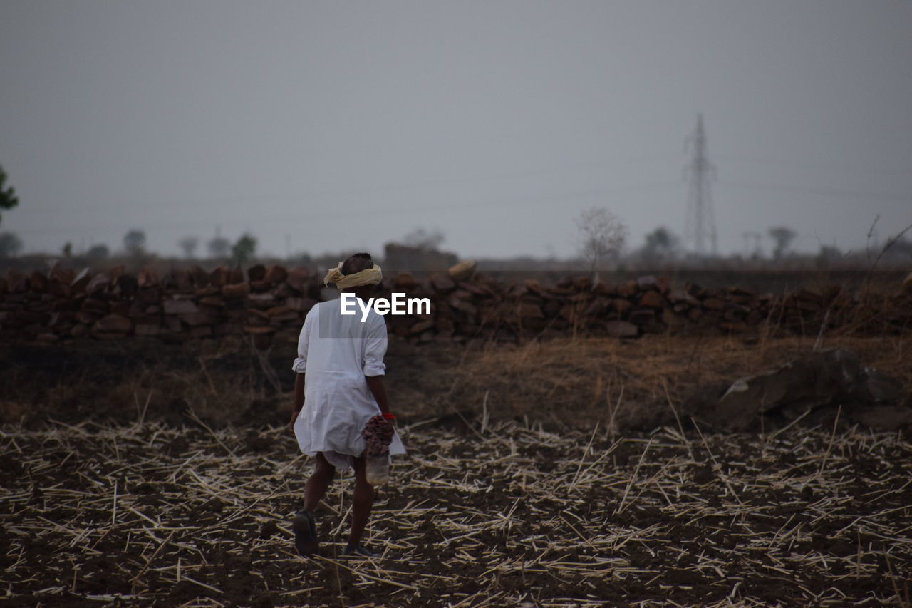 Rear view of man walking on field at dusk