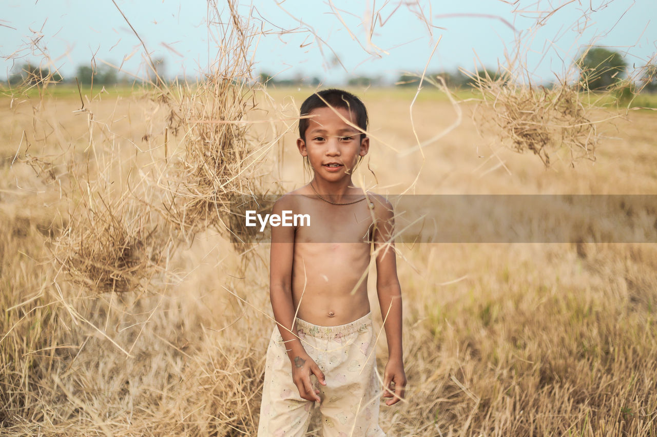 Portrait of boy throwing straws while standing on field at farm against sky