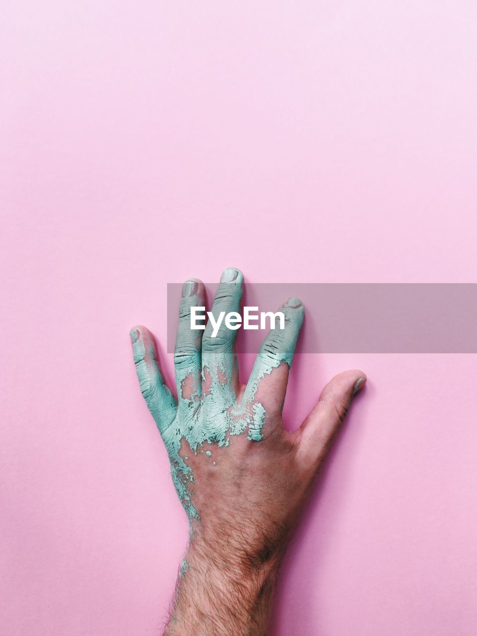 Cropped hand of man with messy paint on pink background