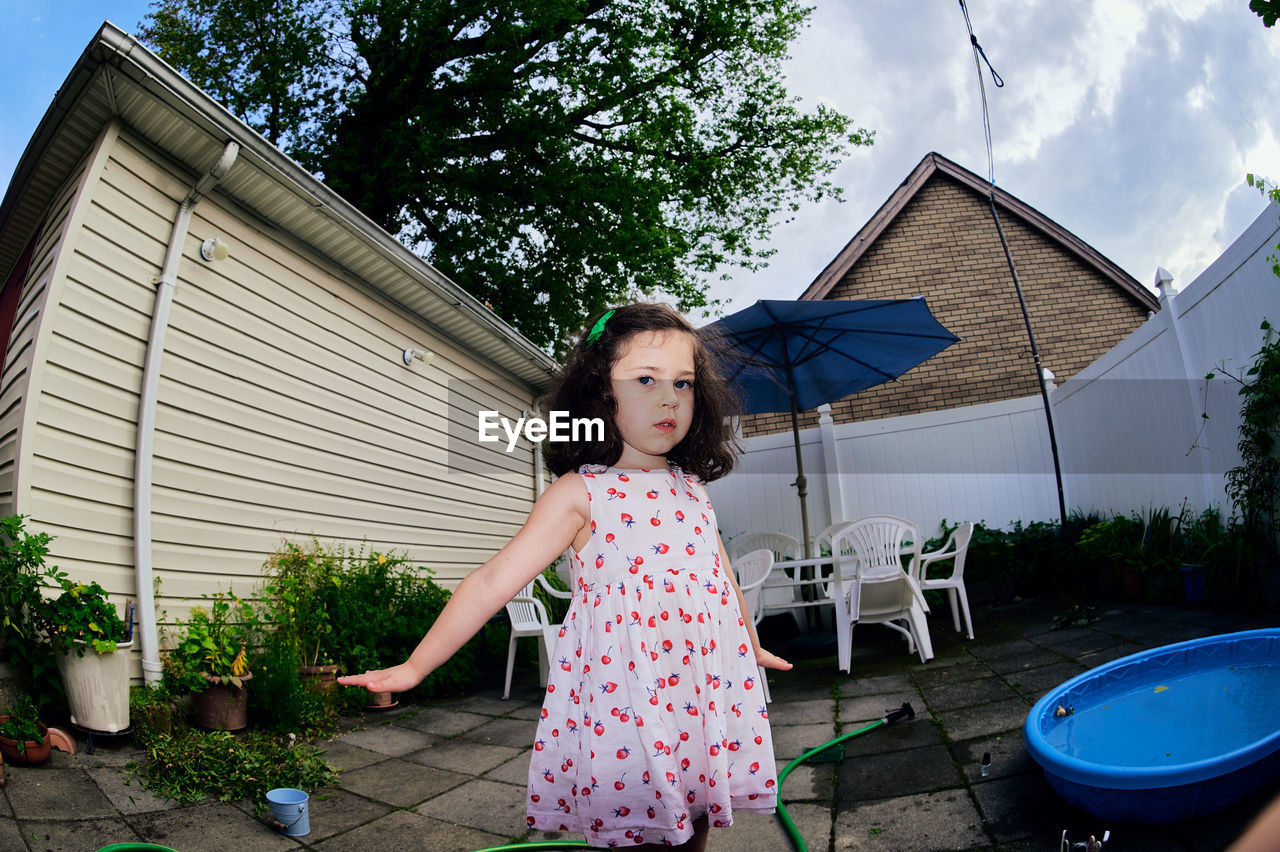 Cute young girl in a summer dress playing in a suburban backyarrd