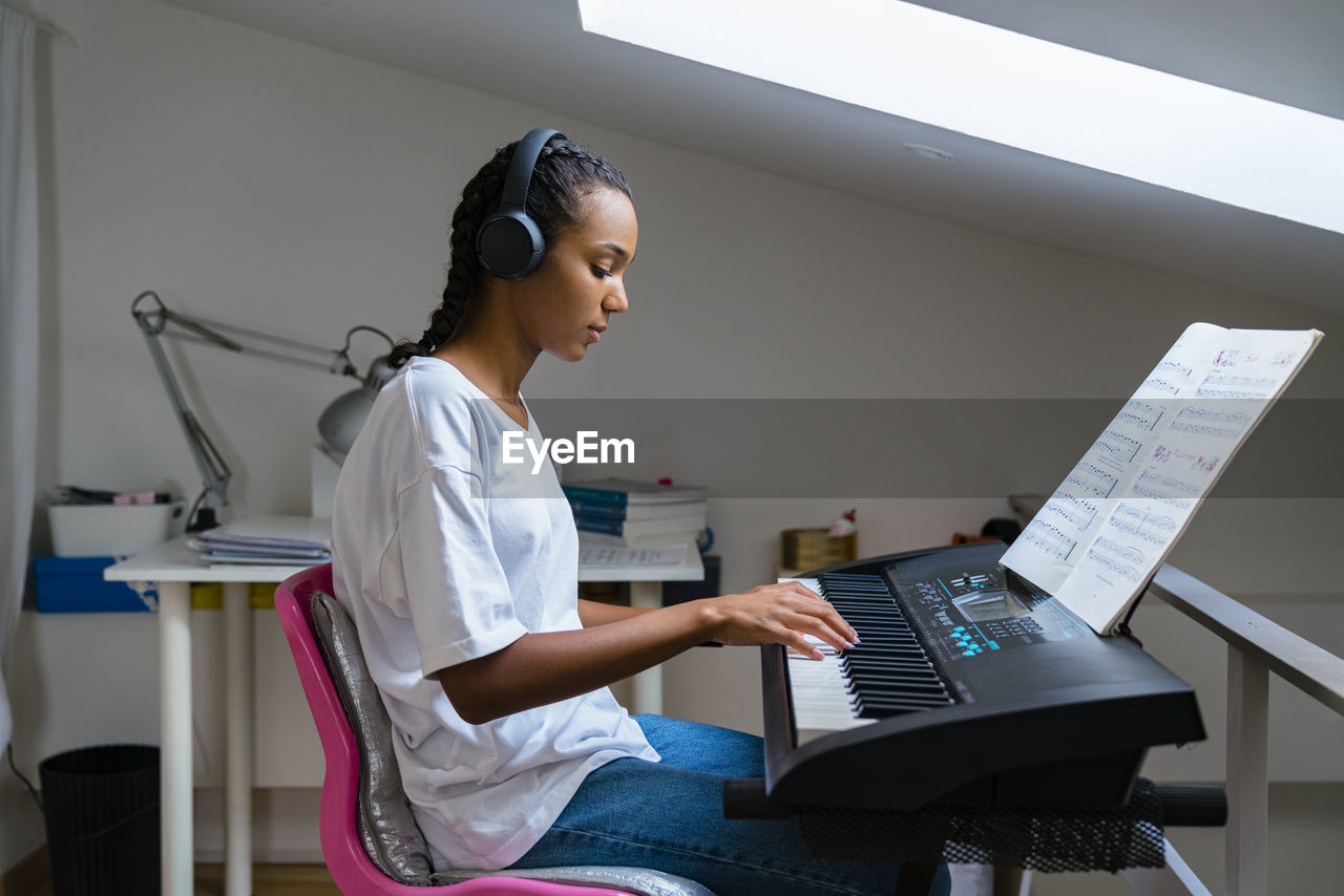 Teenage girl playing piano while sitting at home