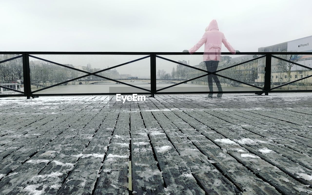 Rear view of woman standing on bridge against sky during winter