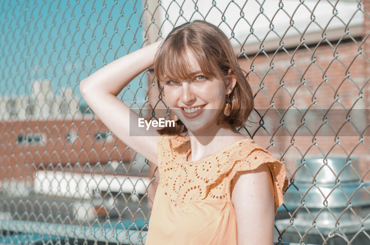 Portrait of smiling woman standing by chainlink fence