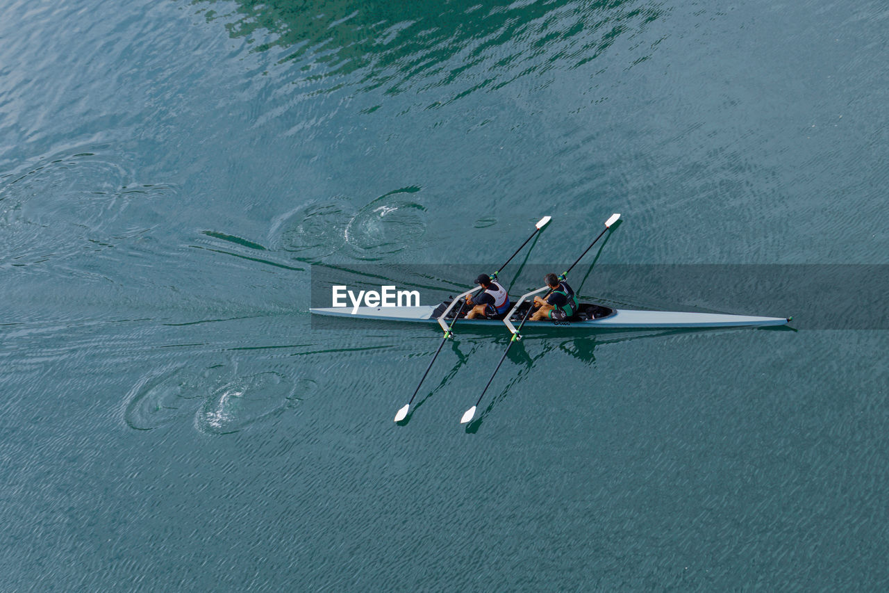 water, nautical vessel, transportation, sports, high angle view, nature, rowing, mode of transportation, men, oar, day, water sports, adult, lake, cooperation, leisure activity, teamwork, outdoors, lifestyles, competition, two people, vehicle, motion, togetherness, blue, adventure, beauty in nature, wing