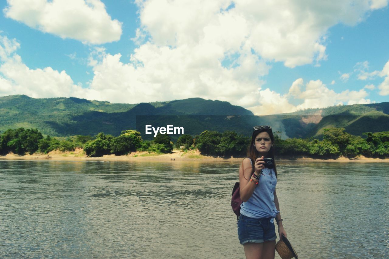 Young woman standing by lake against sky