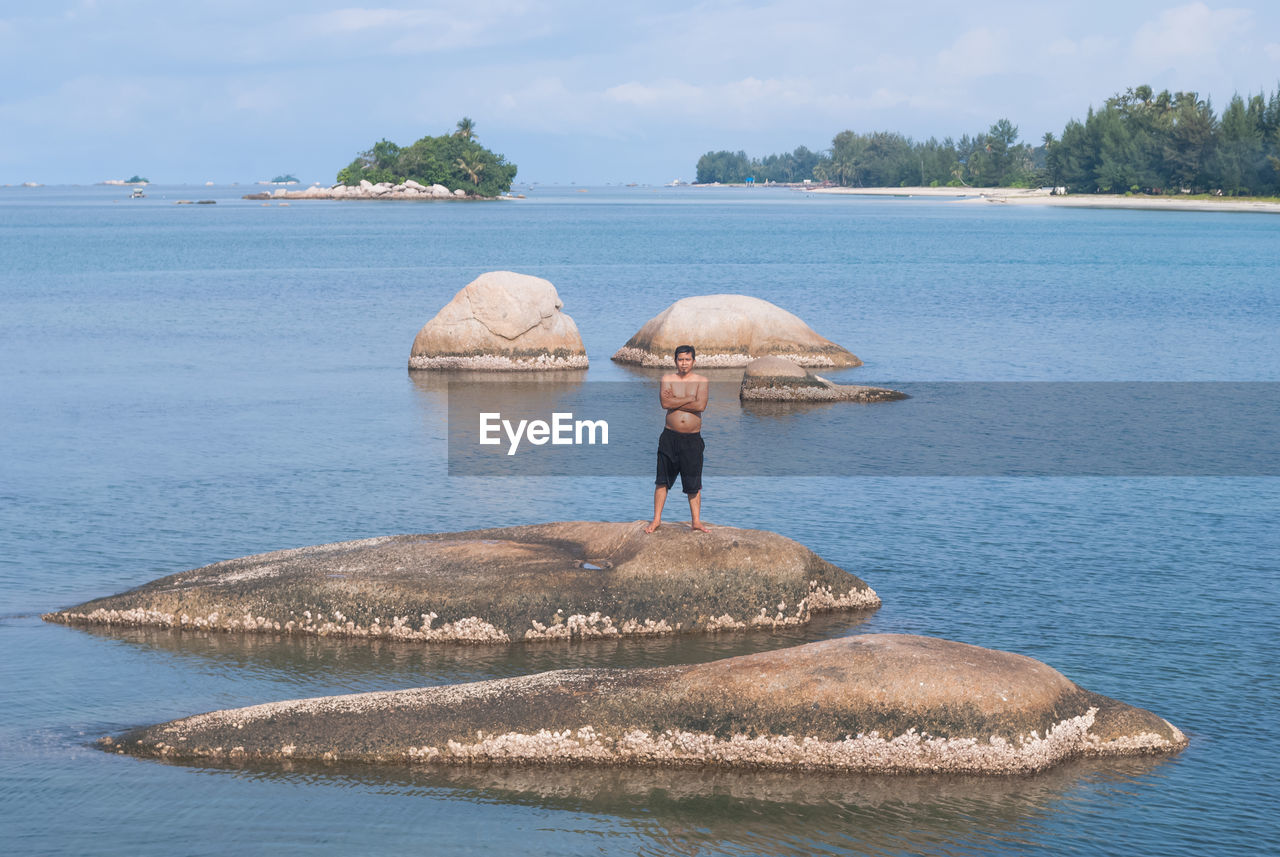 Shirtless man standing on rock amidst river