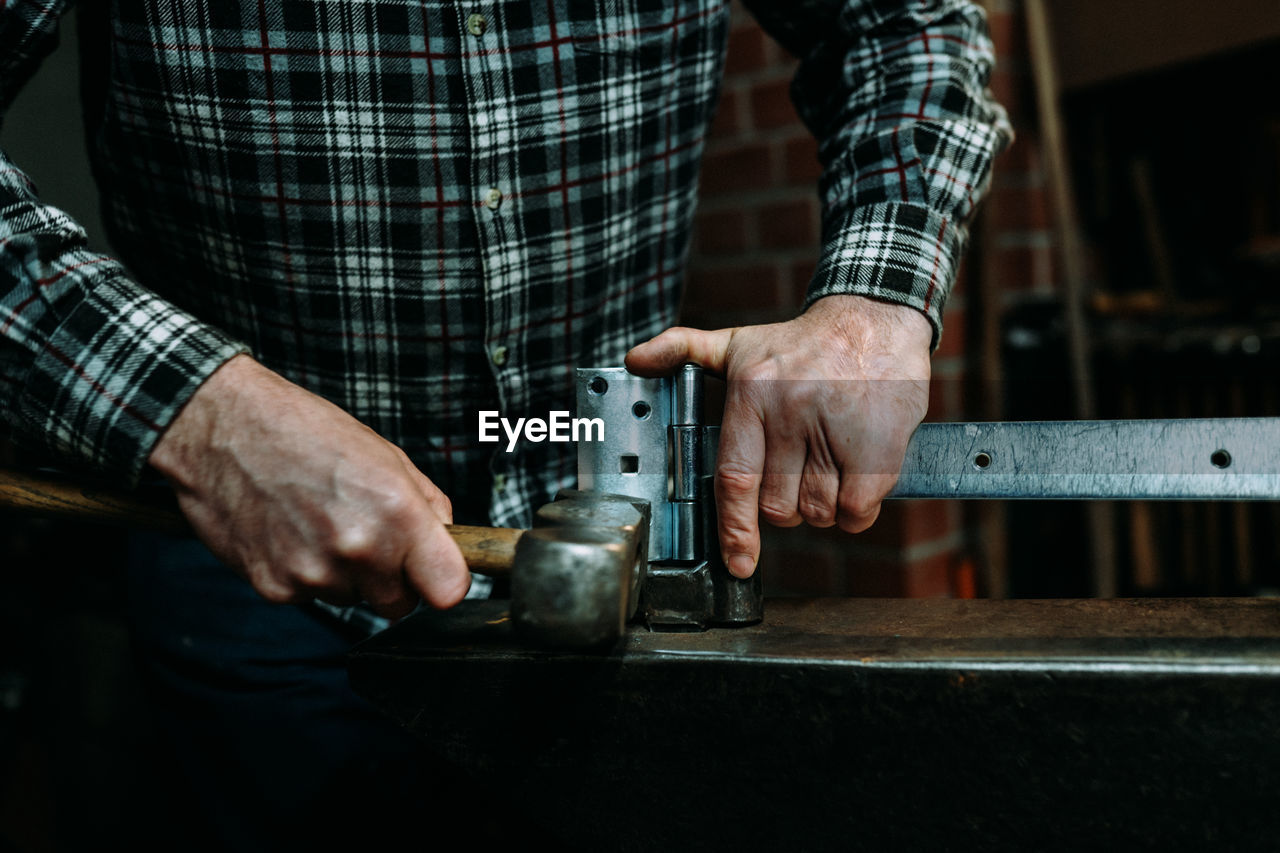 Midsection of man hammering latch in workshop