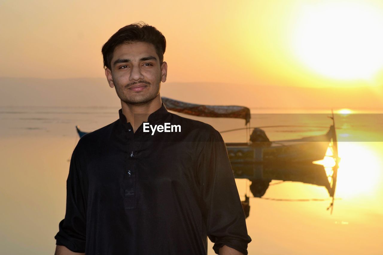 PORTRAIT OF YOUNG MAN STANDING AGAINST ORANGE SKY