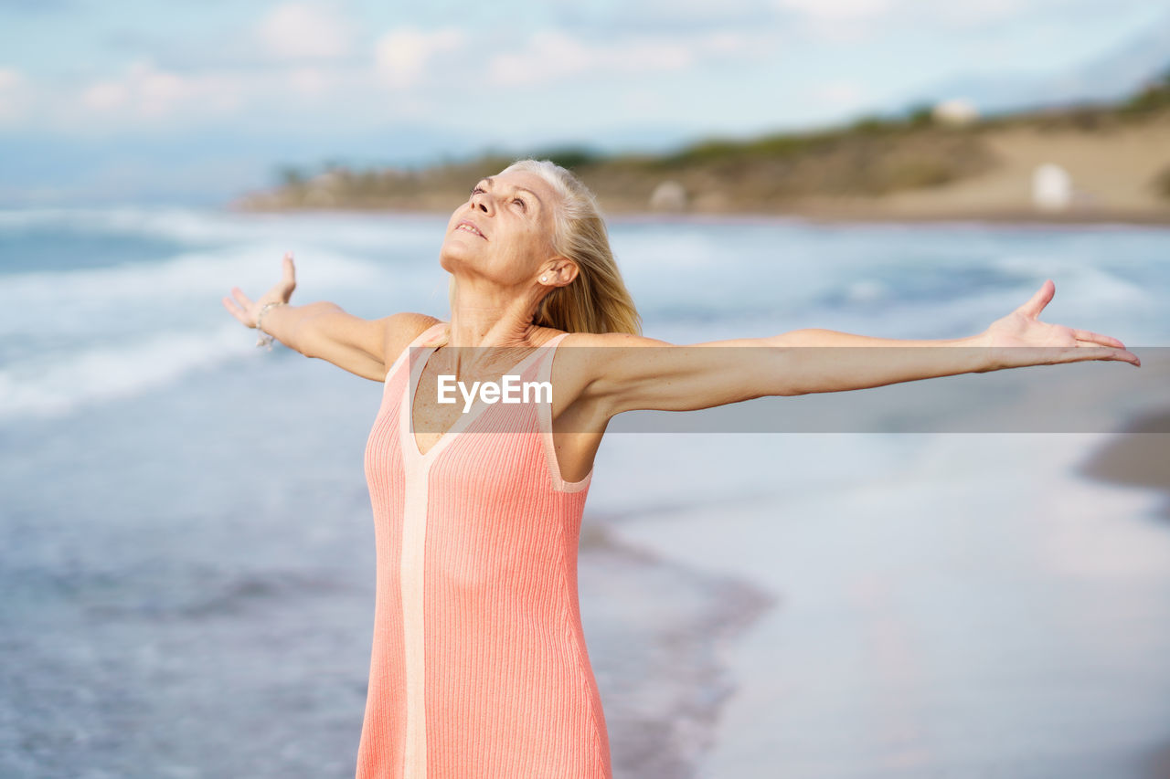 Senior woman with arms outstretched on beach