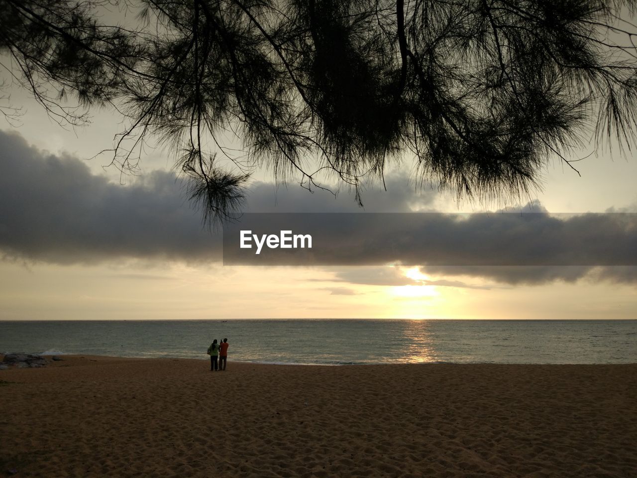 People standing on beach against sky during sunset