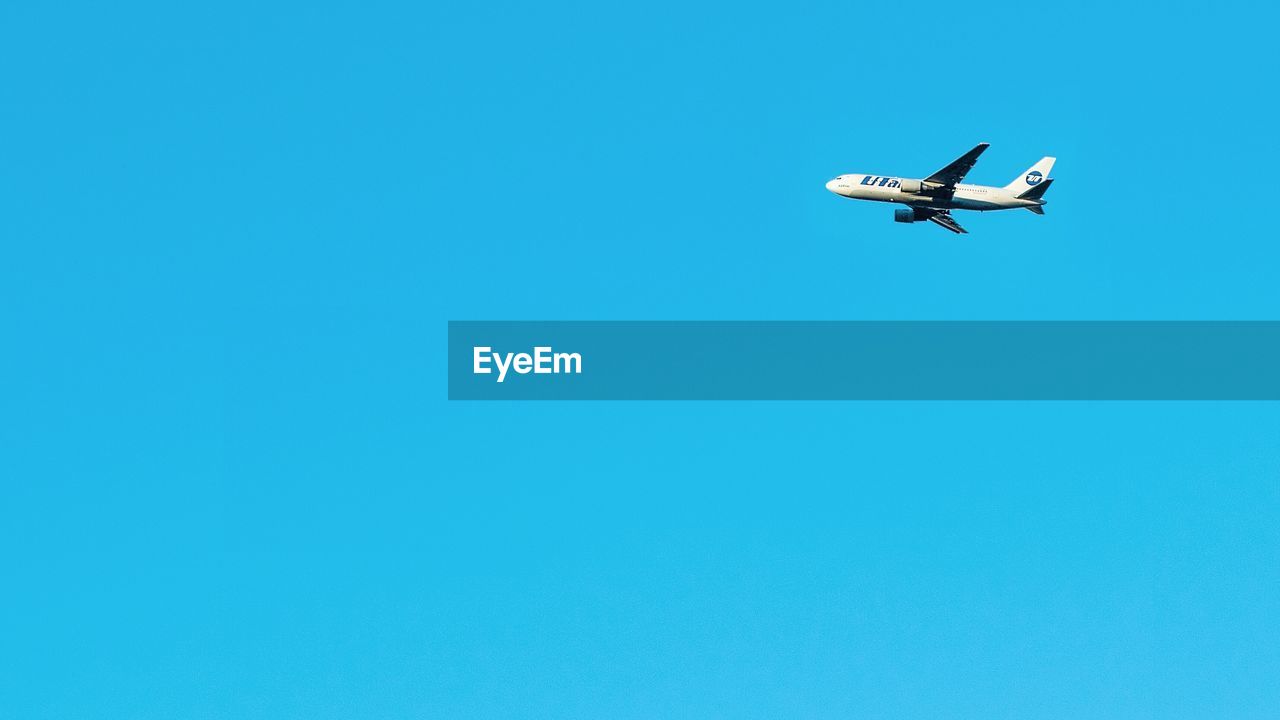 LOW ANGLE VIEW OF AIRPLANE FLYING IN CLEAR BLUE SKY