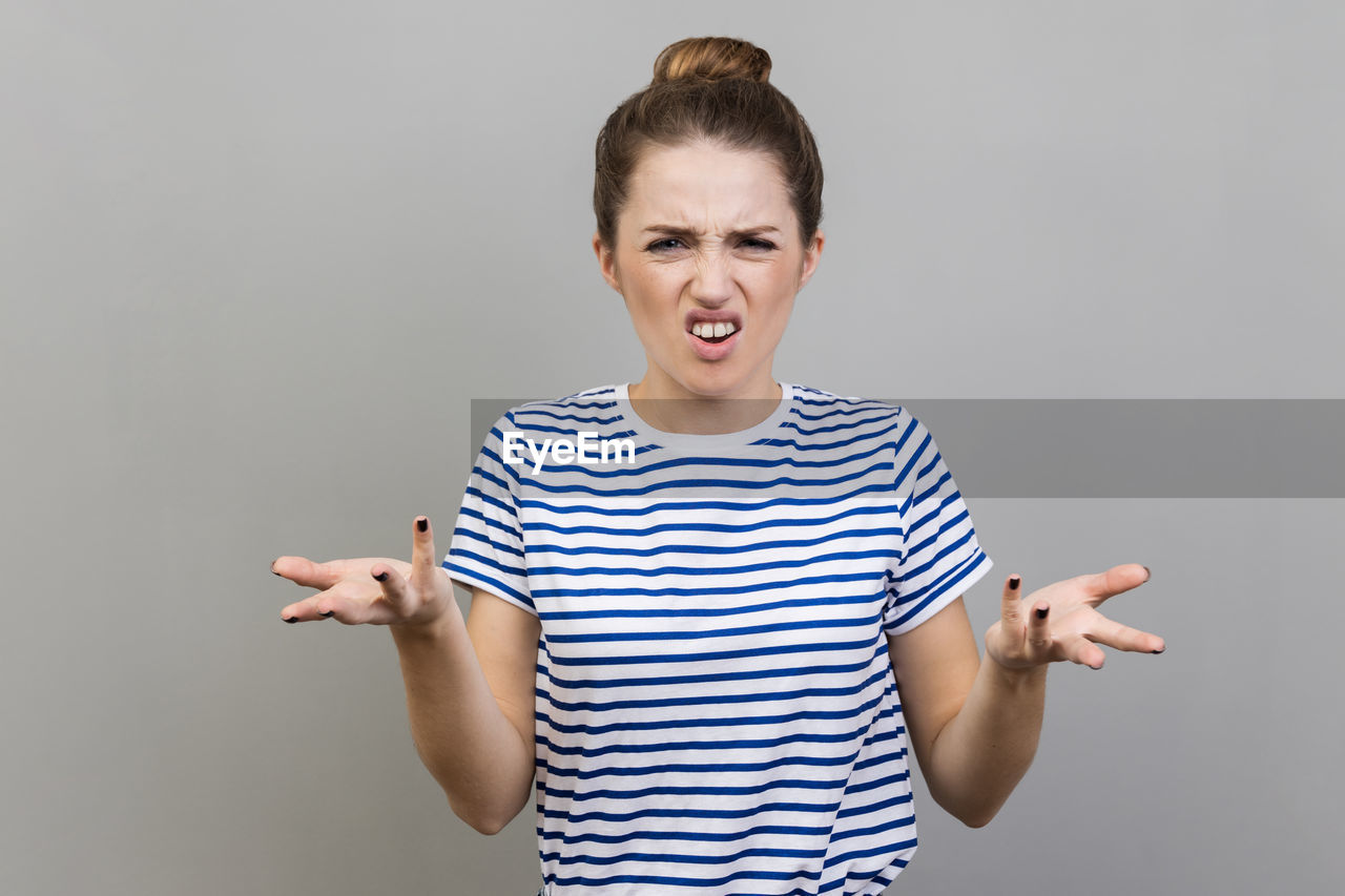 striped, studio shot, one person, emotion, indoors, gesturing, portrait, gray background, casual clothing, adult, mouth open, shouting, facial expression, young adult, gray, front view, person, happiness, standing, waist up, smiling, t-shirt, communication, looking at camera, positive emotion, hand, excitement, anger, negative emotion, fun, finger, colored background, human mouth, teenager, arm, copy space, women, clothing, photo shoot, sleeve, cheerful, sign language, human face, limb, surprise, making a face, human limb, humor, blond hair, hairstyle
