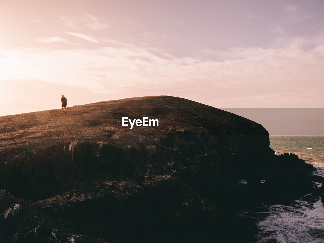 Rear view of man walking on mountain against sky during sunset