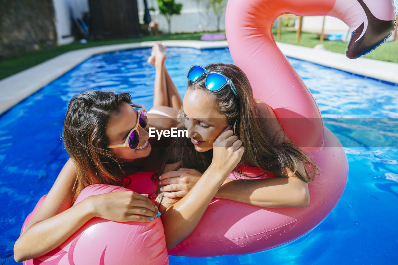 Two young women with pink flamingo float in swimming pool