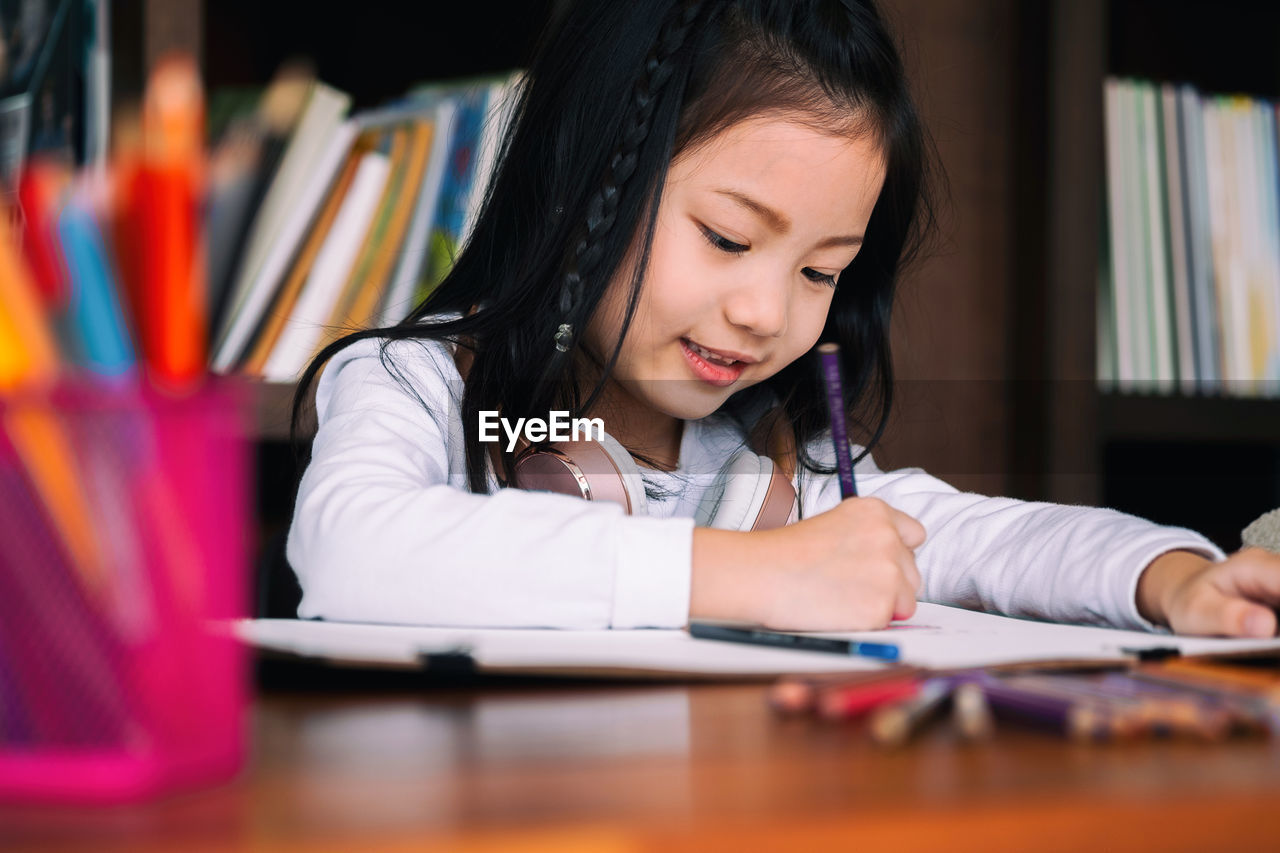 Close-up of girl writing on book at desk