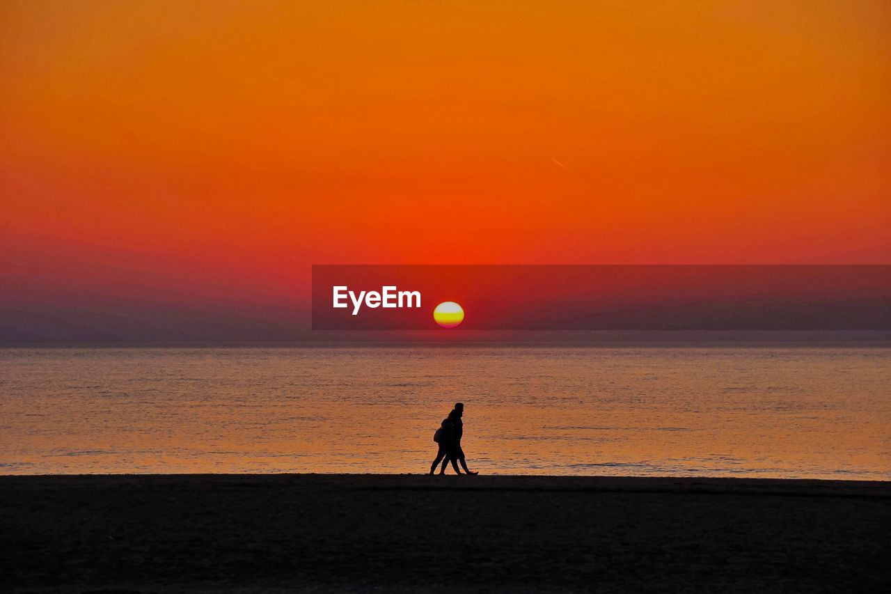 Silhouette people walking at beach during sunset