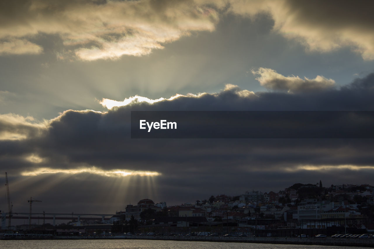 Cityscape by tagus river against cloudy sky during sunset