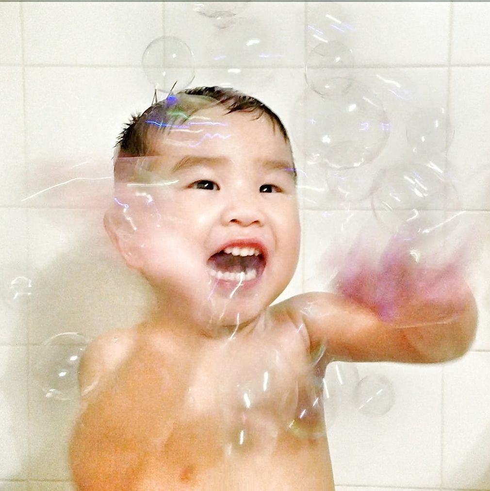 Happy shirtless boy playing with bubbles against wall in bathroom