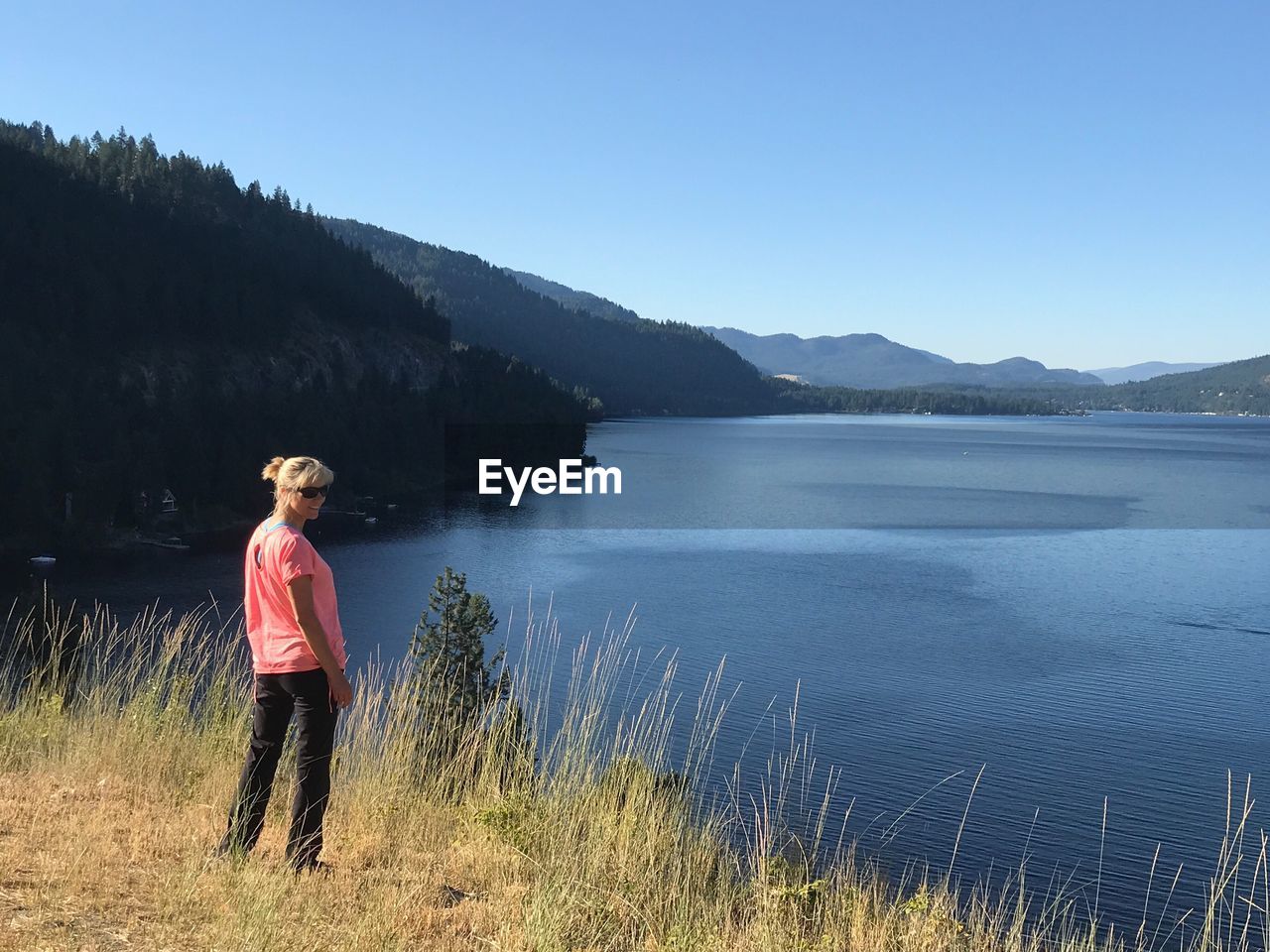 Woman standing by lake against clear blue sky