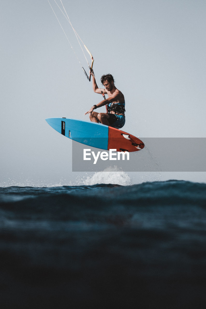 Side view of man kiteboarding in sea against clear sky