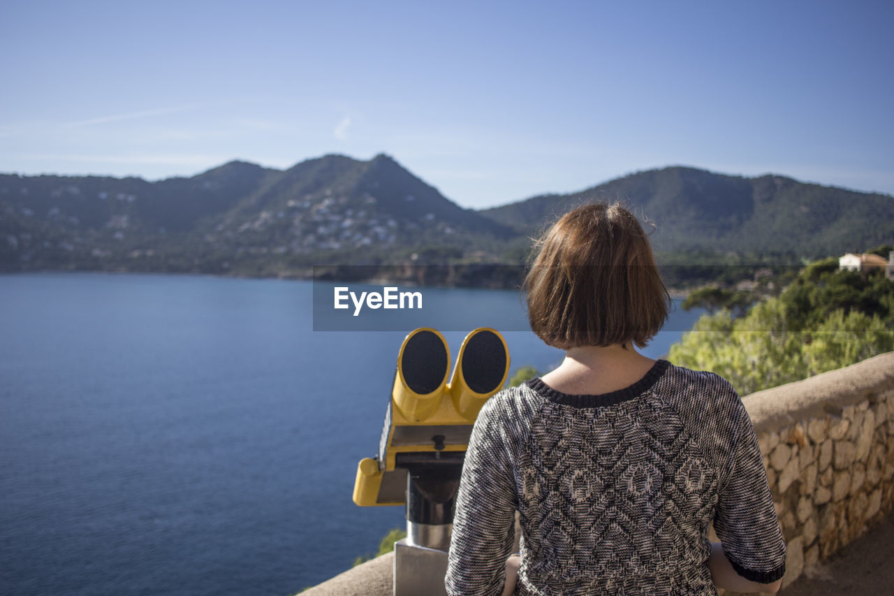 Rear view of woman standing by coin-operated binoculars at observation point against mountain