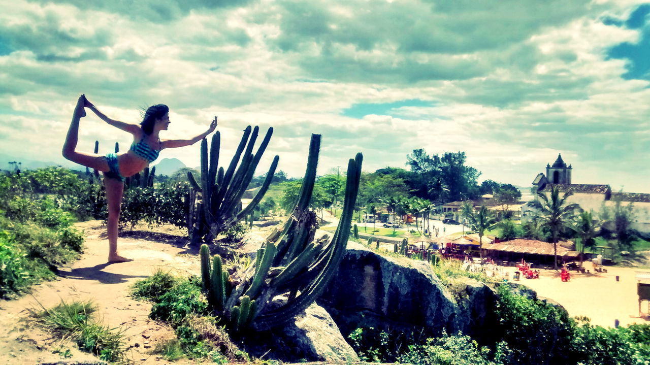 Woman practicing yoga by cactus plants against cloudy sky