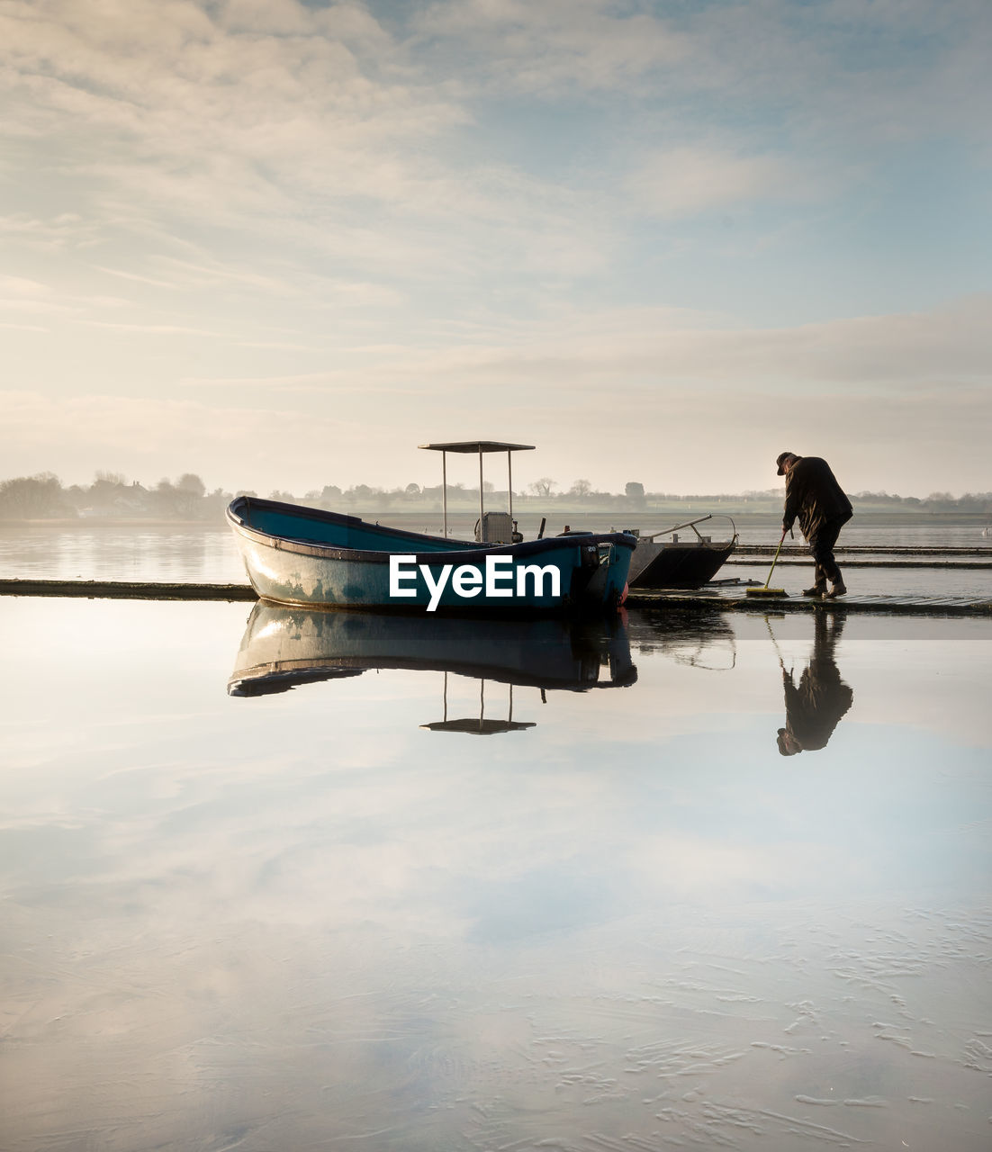 MAN ON BOAT MOORED AGAINST SKY AT SUNSET