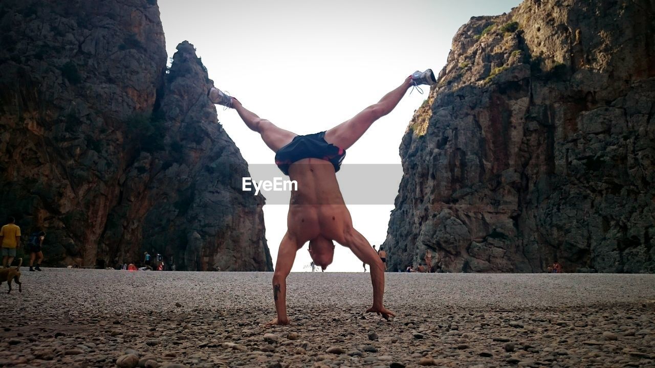 Shirtless man performing handstand at beach