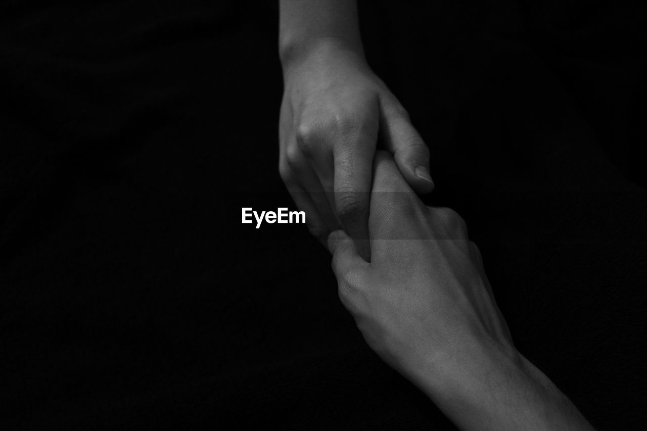 Cropped image of people holding hands against black background