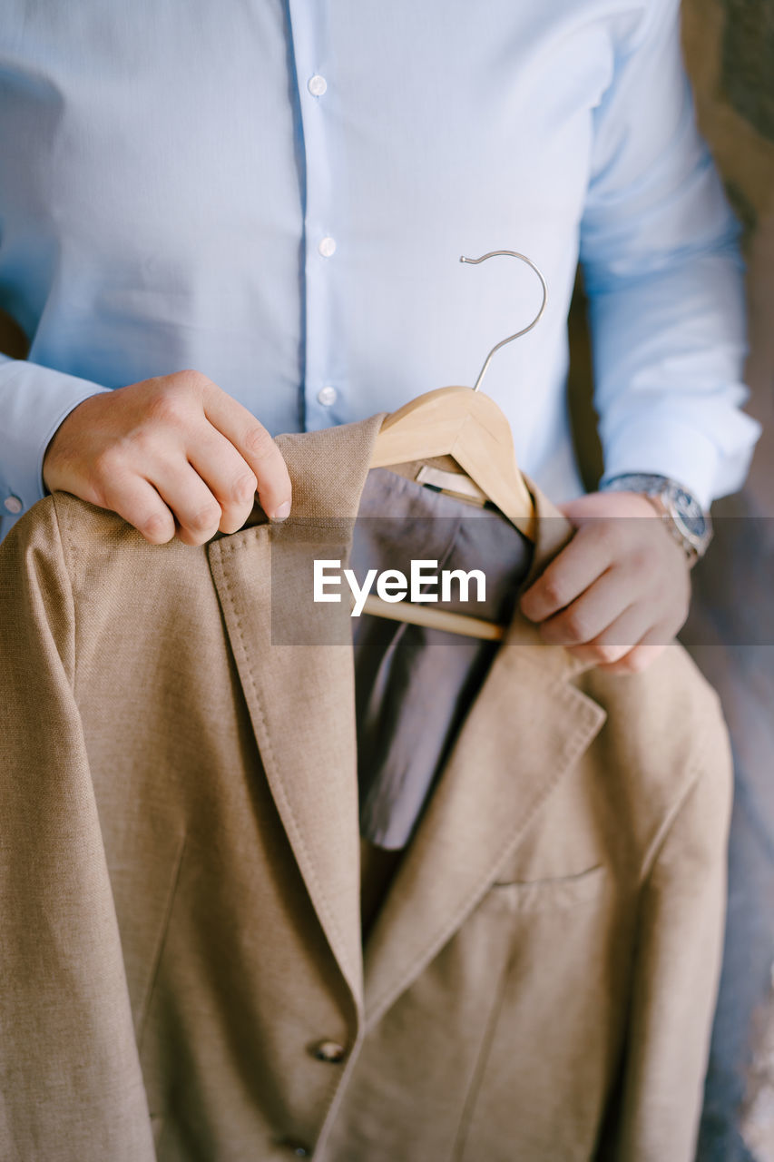 MIDSECTION OF MAN HOLDING HANDS WHILE STANDING IN KITCHEN