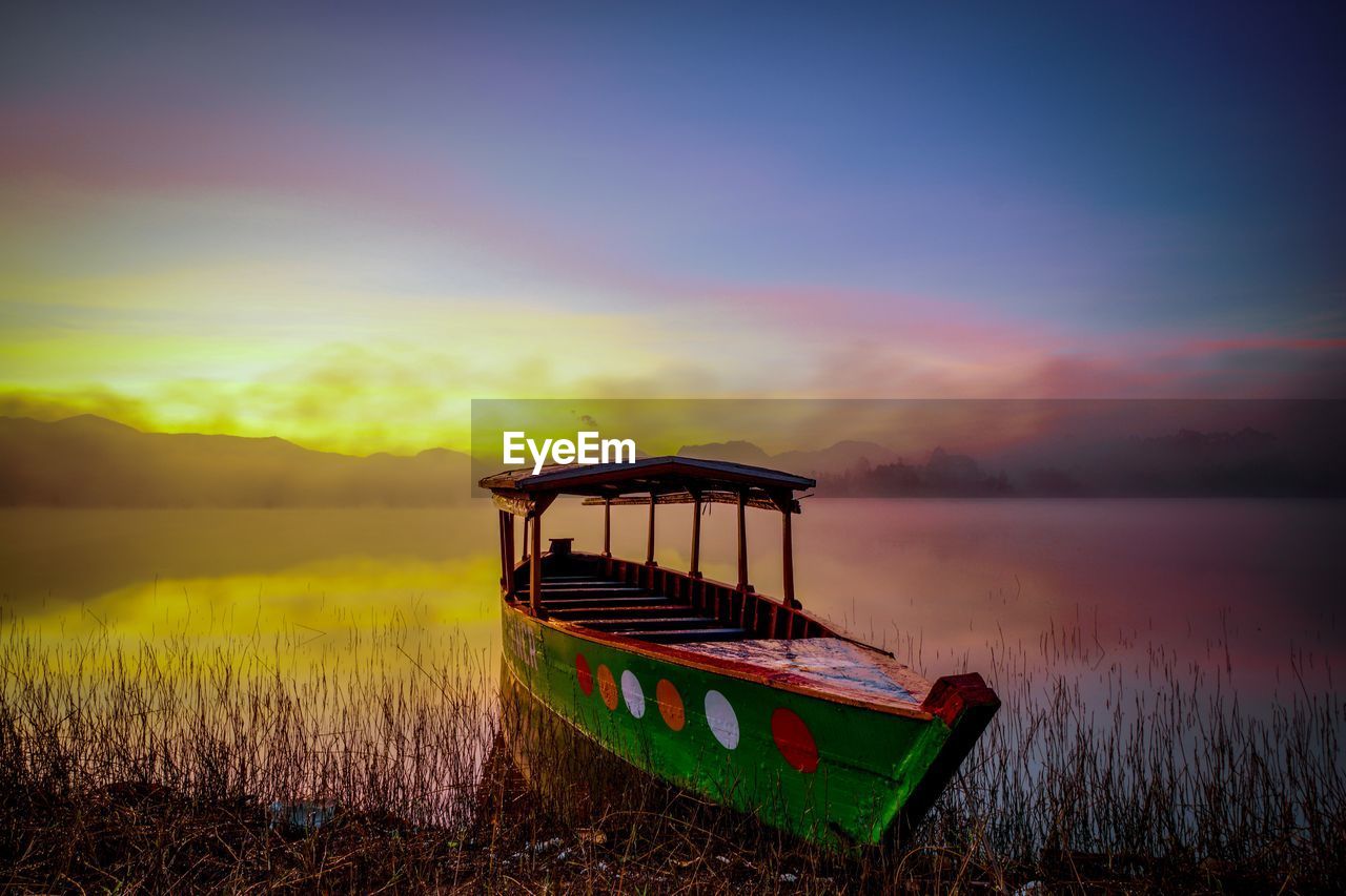 Boat moored in lake against sky during sunset