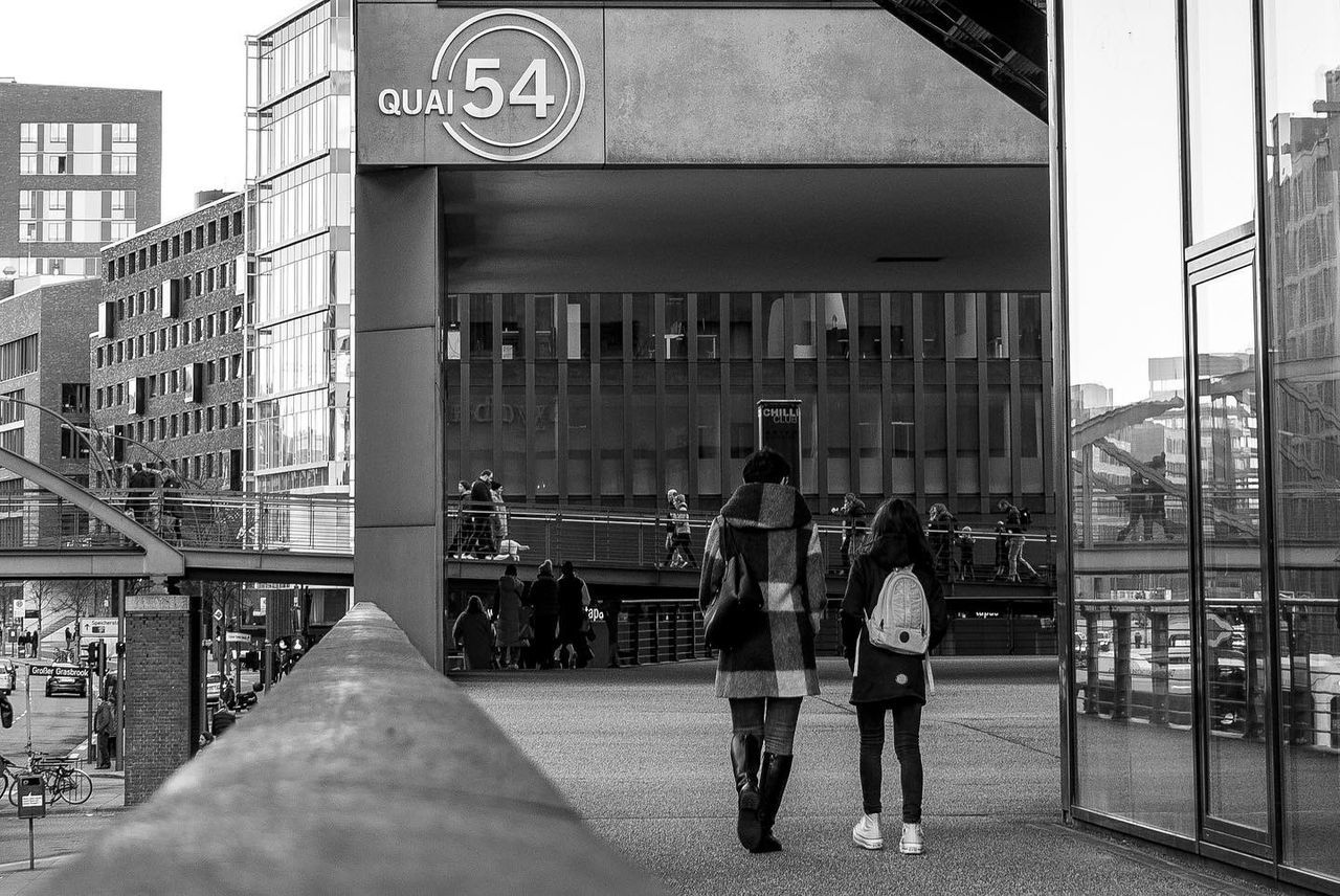 architecture, black and white, built structure, building exterior, city, street, monochrome, monochrome photography, road, group of people, men, adult, building, urban area, women, city life, full length, lifestyles, day, walking, transportation, infrastructure, leisure activity, outdoors, communication, sign, downtown