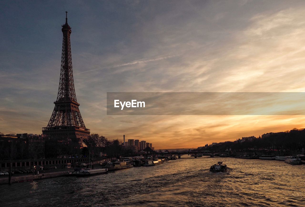 Eiffel tower by river against sky during sunset