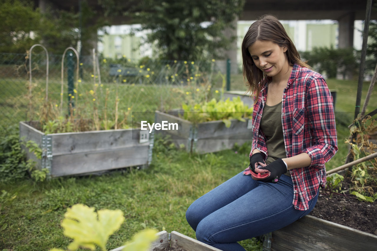 Mid adult woman sitting on edge of wooden crate at urban garden