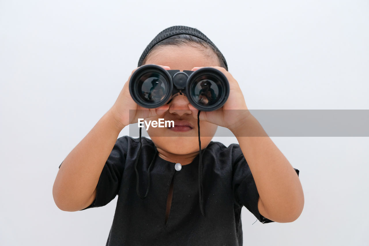 Portrait of boy looking through binoculars against white background