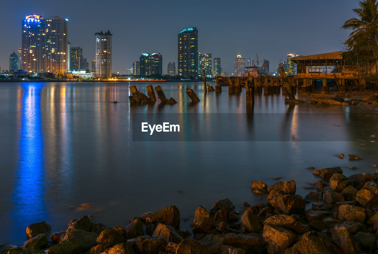 Illuminated buildings by chao phraya river against sky