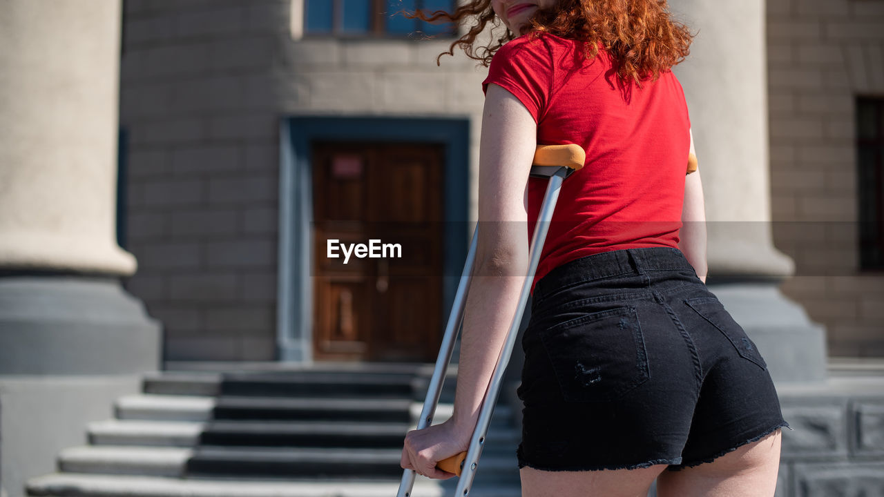 REAR VIEW OF WOMAN STANDING AT BUILDING