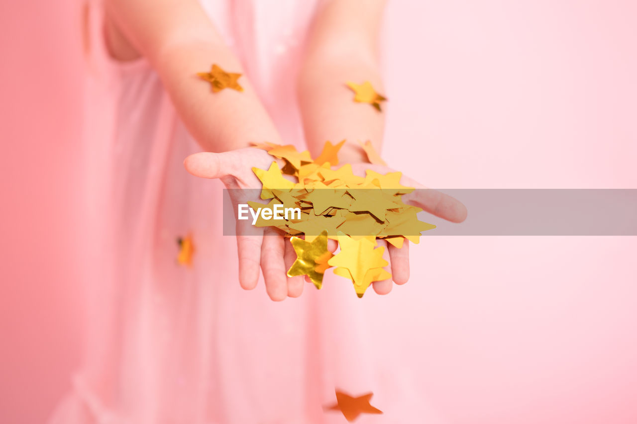 Close up of child hands with gold confetti. kid in pink dress celebrating birthday