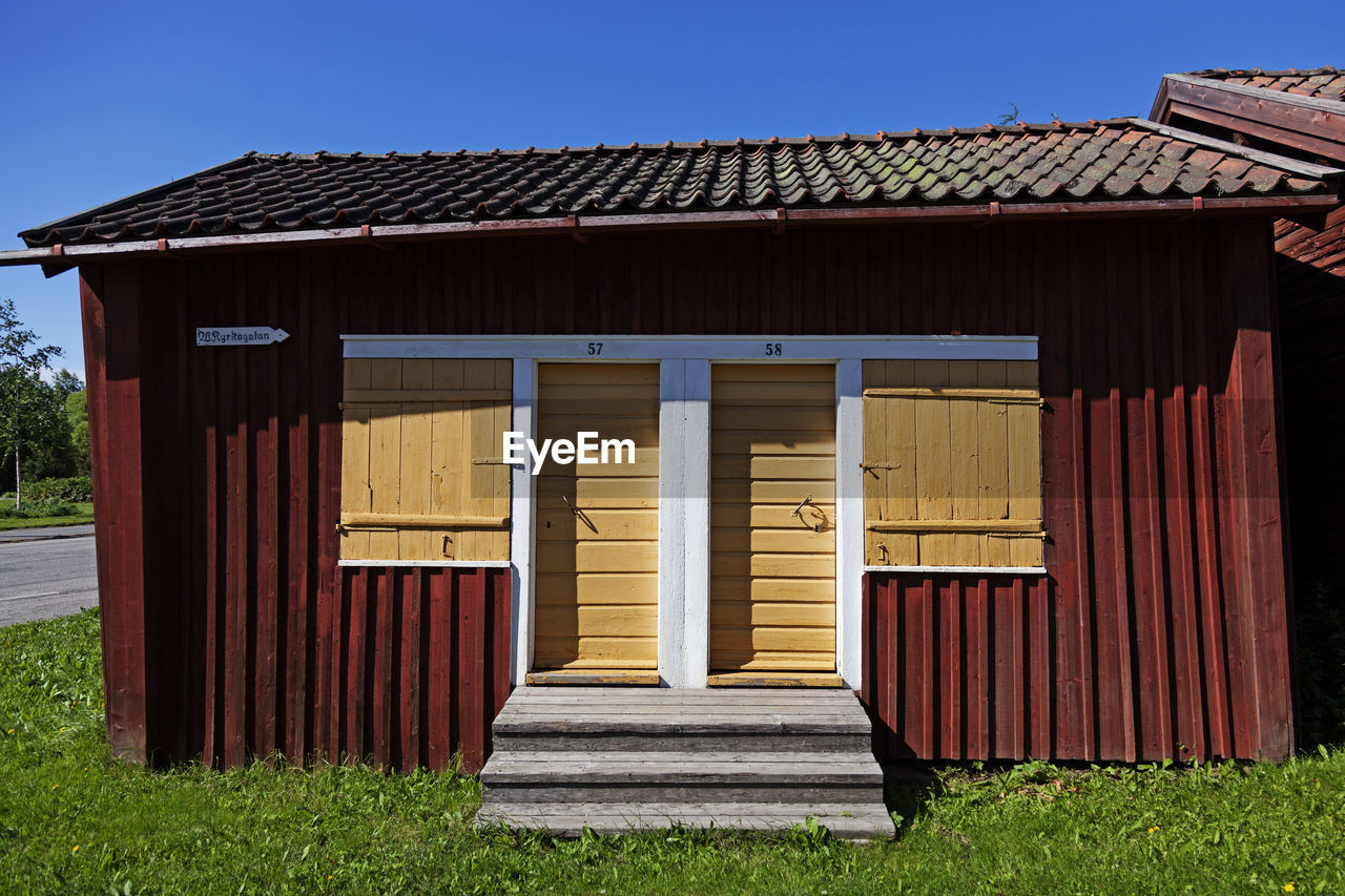 architecture, built structure, building exterior, shed, grass, house, building, nature, sky, facade, no people, plant, wood, outdoor structure, home, clear sky, log cabin, day, blue, outdoors, barn, land, hut, landscape, residential district, roof, sunny, shack, rural scene, entrance