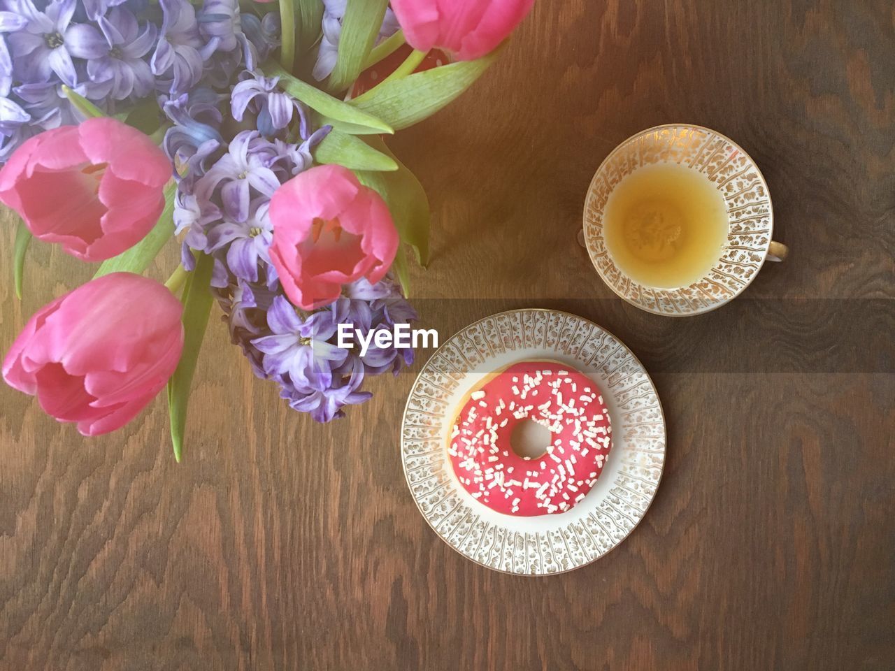 High angle view of donut with drink served by flowers vase on wooden table