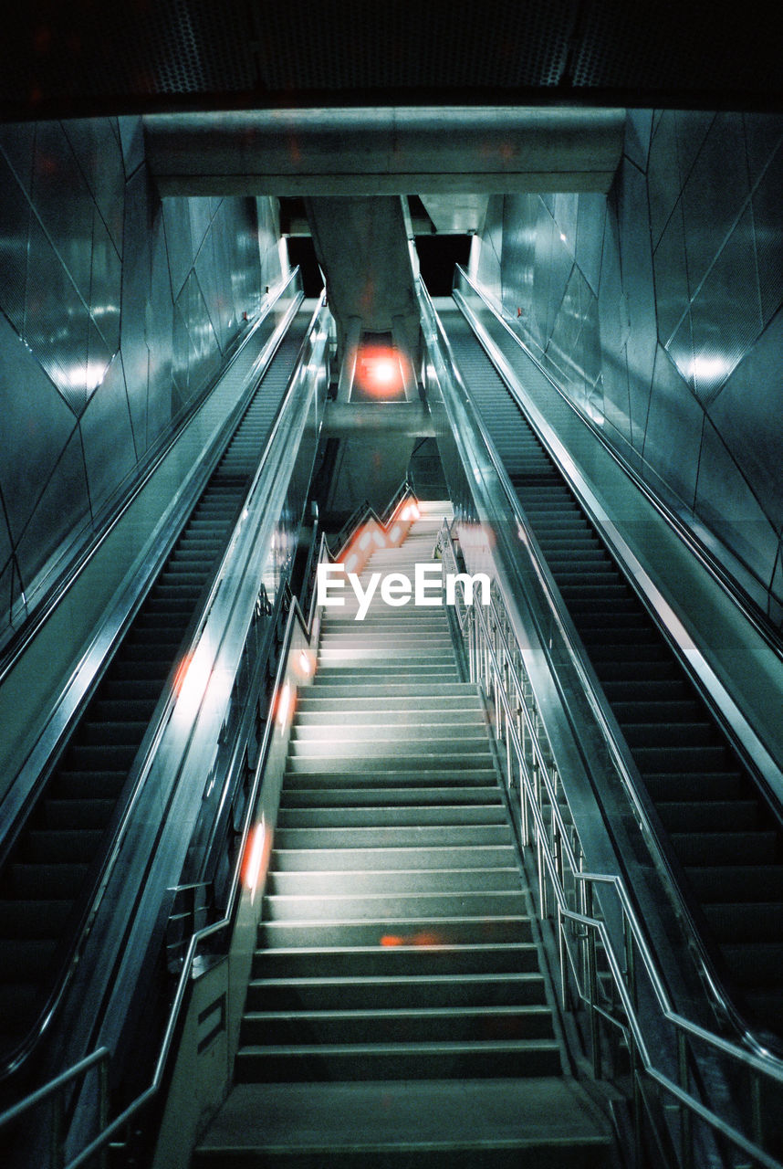 HIGH ANGLE VIEW OF ESCALATOR IN ILLUMINATED UNDERGROUND