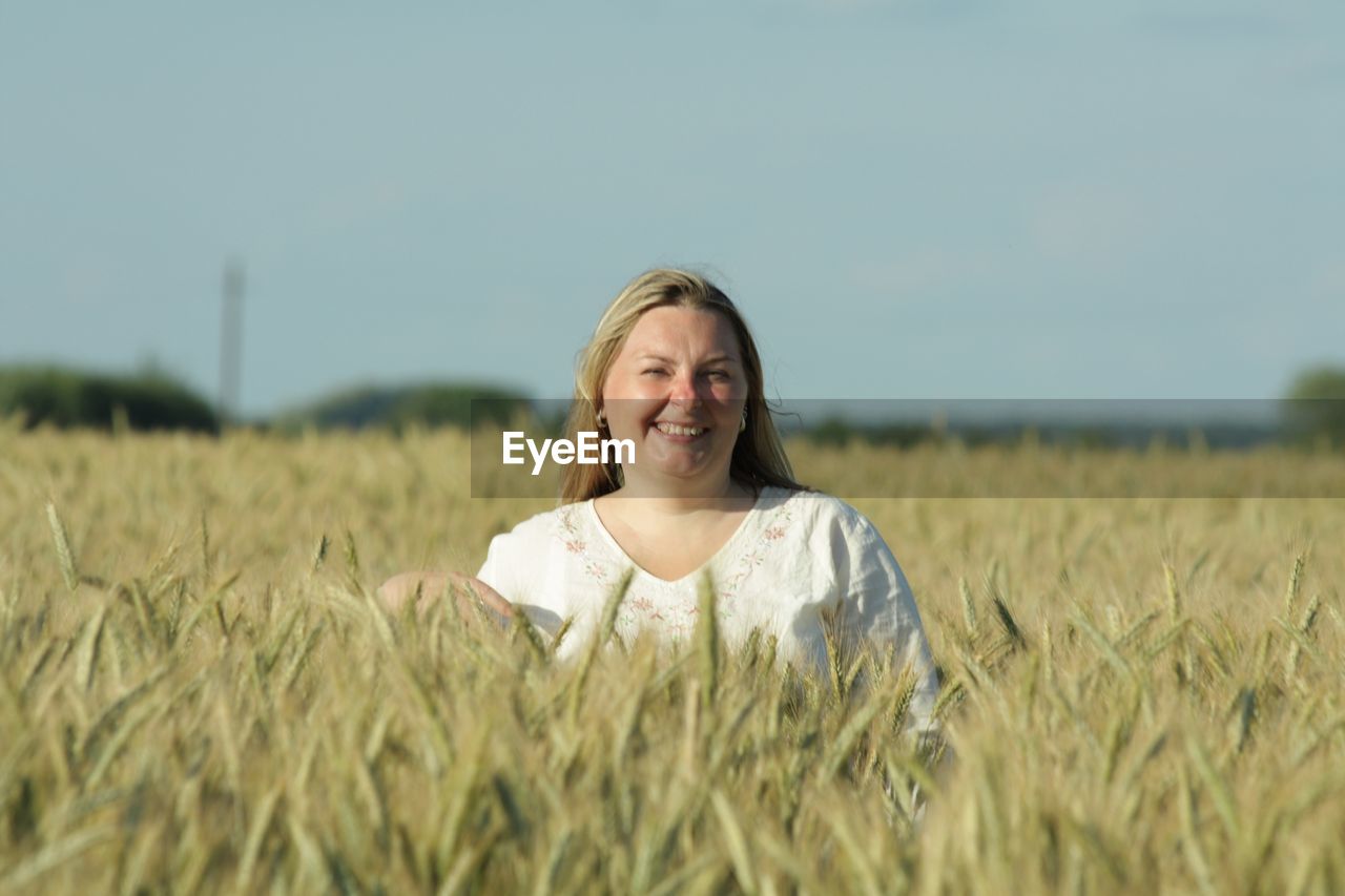 Portrait of smiling woman standing amidst crops against clear sky