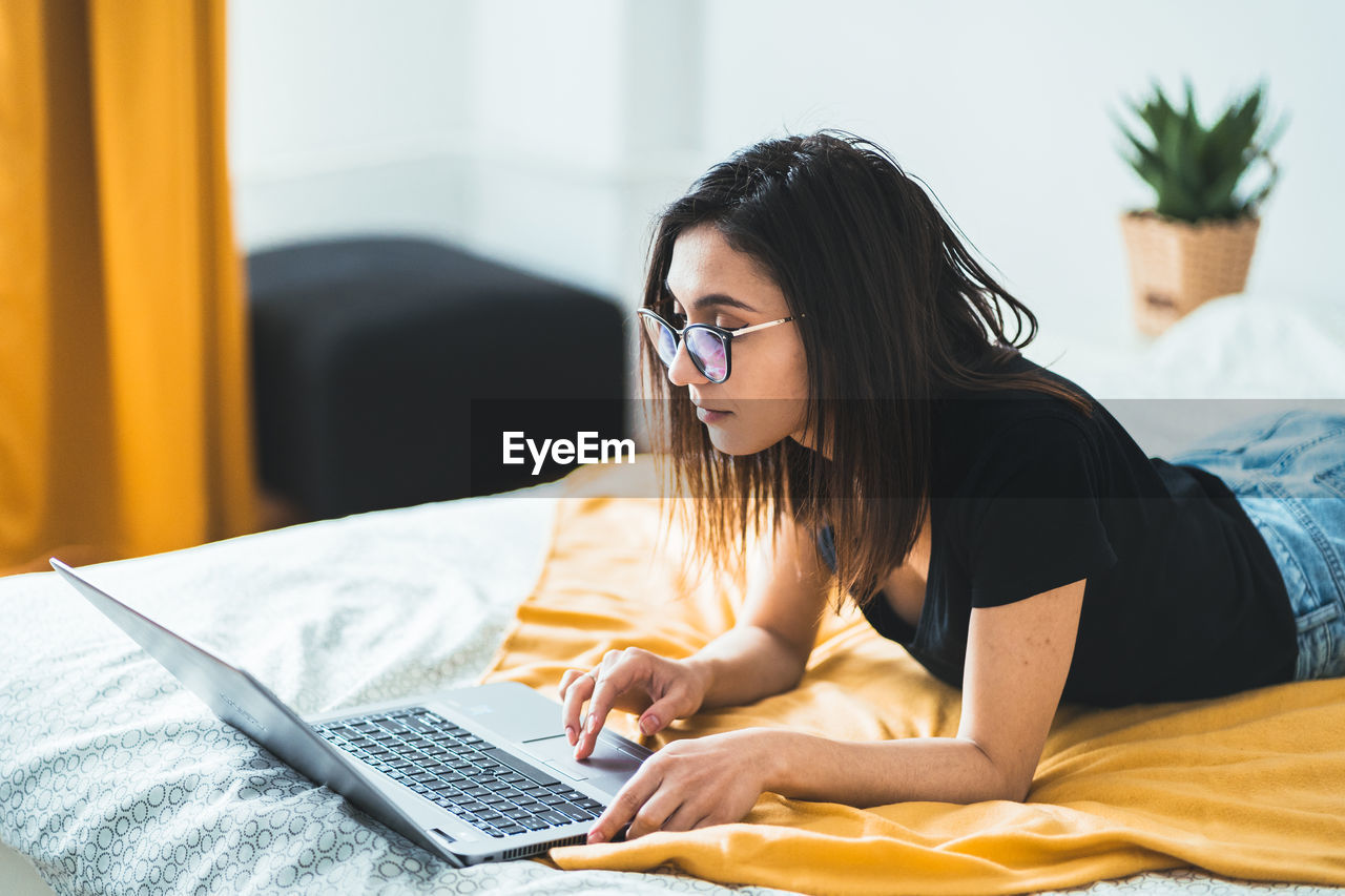 Female lying in bed at home using laptop touchpad. freelance lifestyle and work from home concept.